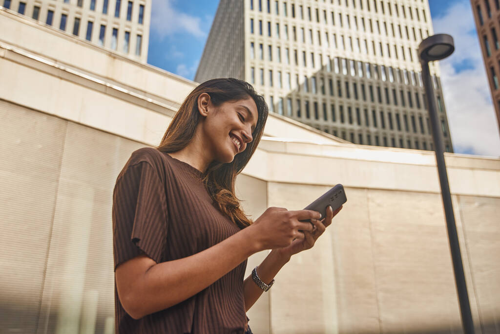 Young and smiling businesswoman standing on street when text messaging - Photo, Image