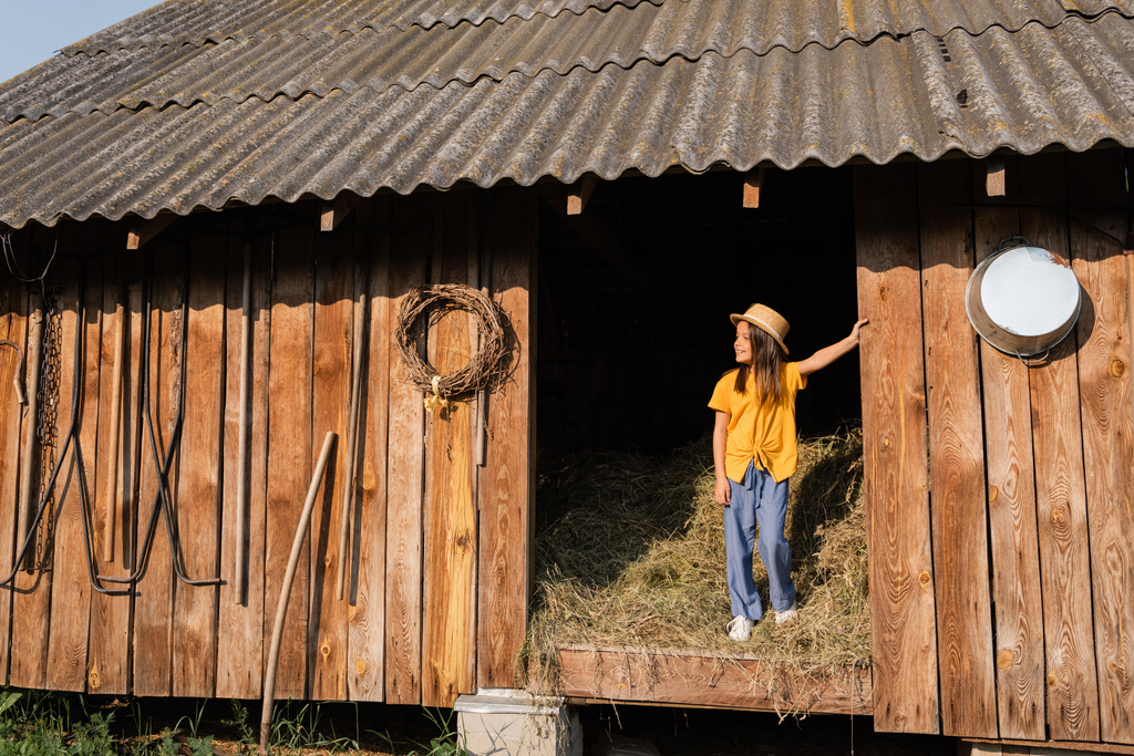 full length of girl standing on hey in wooden barn and looking away - Foto, Bild