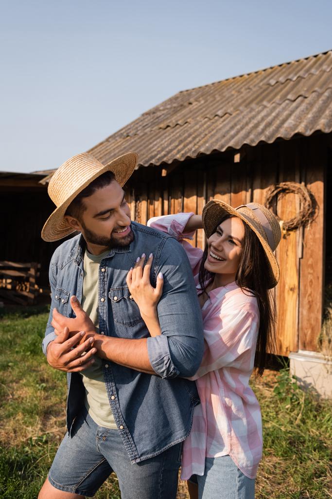 radosna kobieta w słomkowym kapeluszu przytulająca męża na farmie na wsi - Zdjęcie, obraz