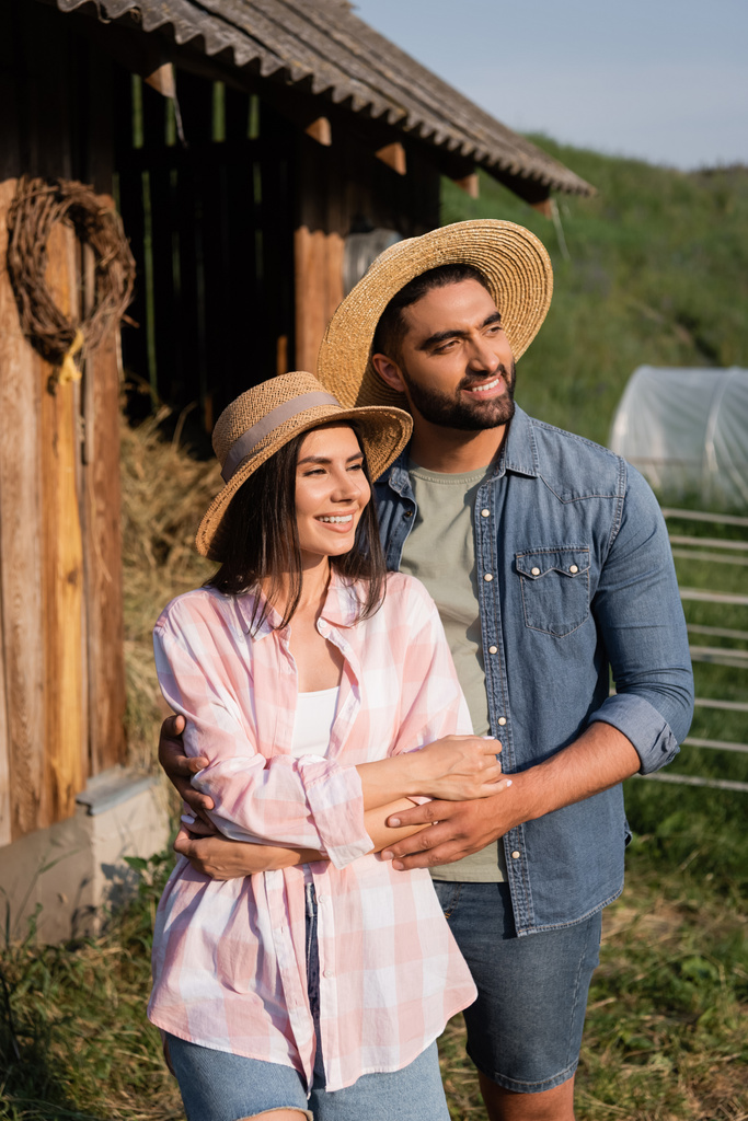 coppia sorridente in cappelli di paglia distogliendo lo sguardo in fattoria in campagna - Foto, immagini
