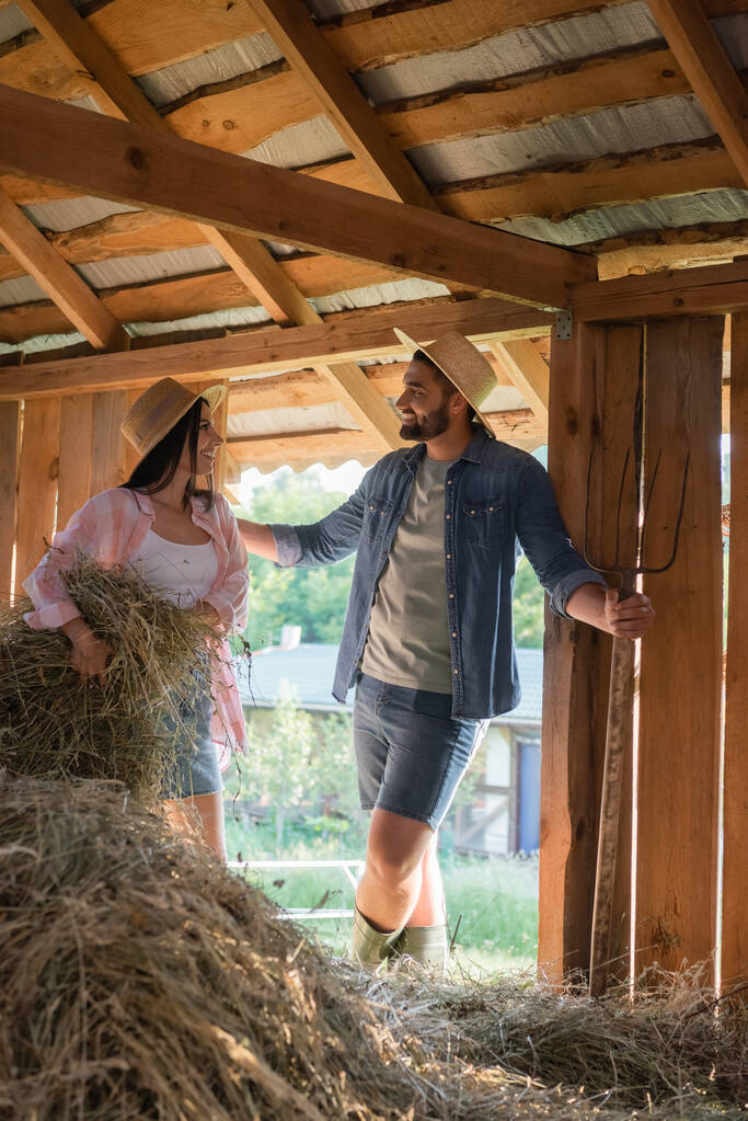 Vidám férfi beszél feleségével halmozás hé pajtában, miközben a farmon dolgozik - Fotó, kép