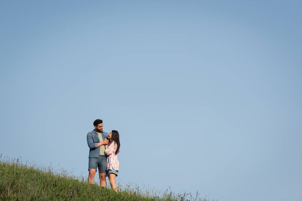 ρομαντικό ζευγάρι κοιτάζονται και αγκαλιάζονται στο πεδίο κάτω από τον γαλάζιο ουρανό - Φωτογραφία, εικόνα
