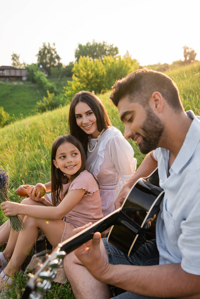 hymyilevä nainen lapsi kuuntelee isä soittaa akustista kitaraa ulkona - Valokuva, kuva