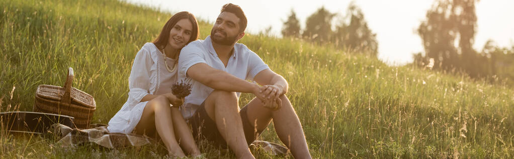pareja complacida sentado y mirando hacia otro lado en el prado en el campo, bandera - Foto, Imagen