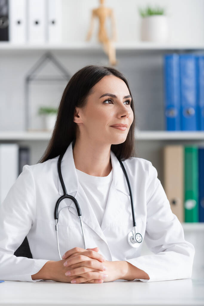 Portrait of brunette doctor looking away in clinic  - Foto, afbeelding