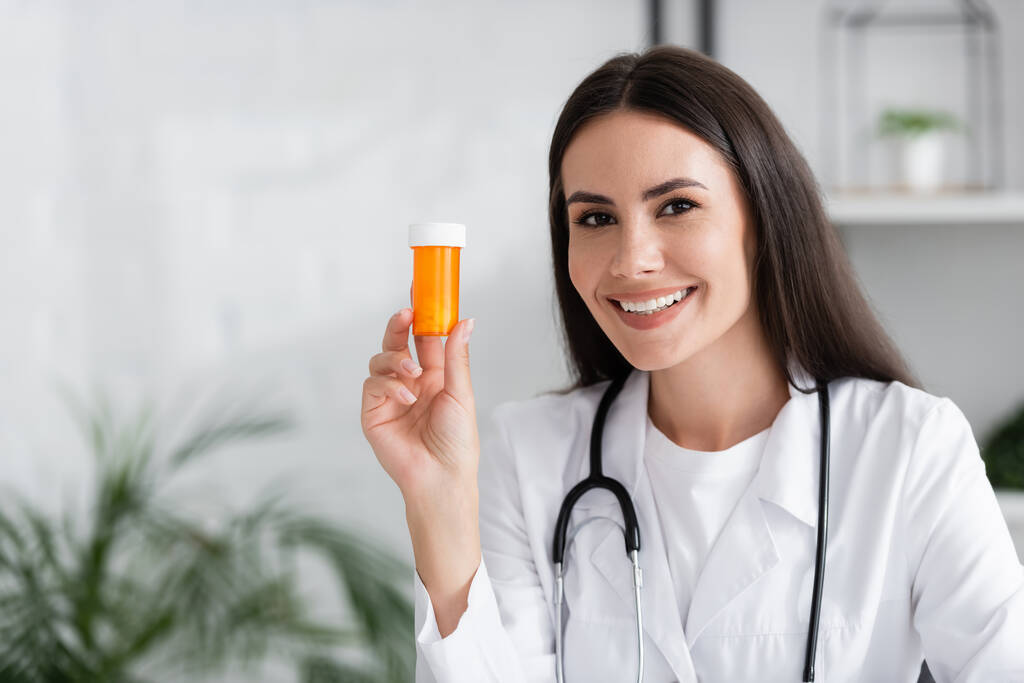 Веселий лікар тримає таблетки і дивиться на камеру в клініці
  - Фото, зображення