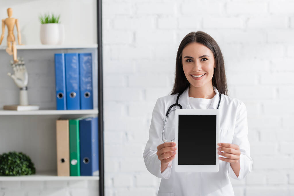 Μελαχρινή γιατρός σε λευκό παλτό κρατώντας ψηφιακό δισκίο στην κλινική  - Φωτογραφία, εικόνα