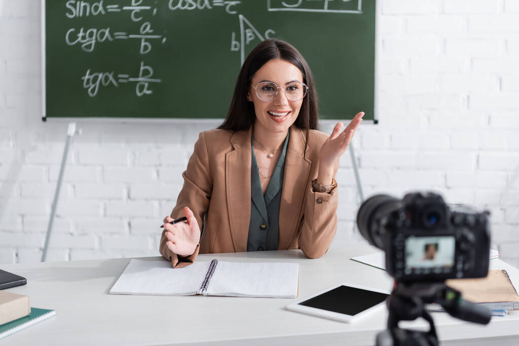 Positive teacher talking near blurred digital camera in classroom  - Fotografie, Obrázek