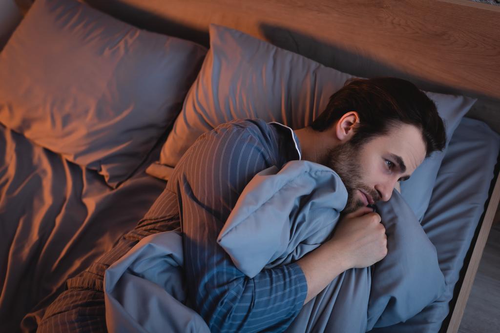 Vue du dessus de l'homme en pyjama souffrant d'insomnie au lit la nuit  - Photo, image
