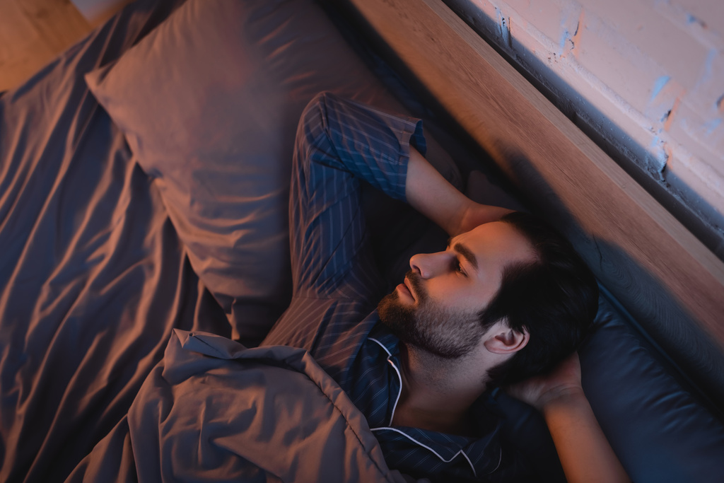 Vista lateral del hombre con trastorno del sueño acostado en la cama en casa  - Foto, imagen