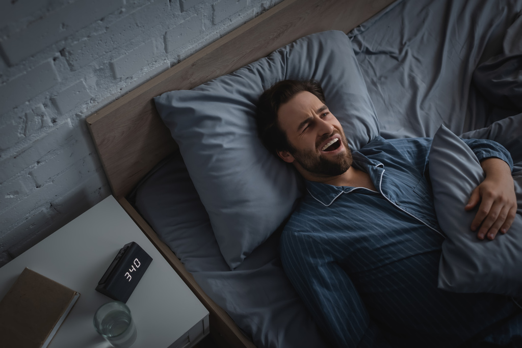 Top view of man with insomnia yawning near clock and water on bedside table in morning - Foto, Imagem