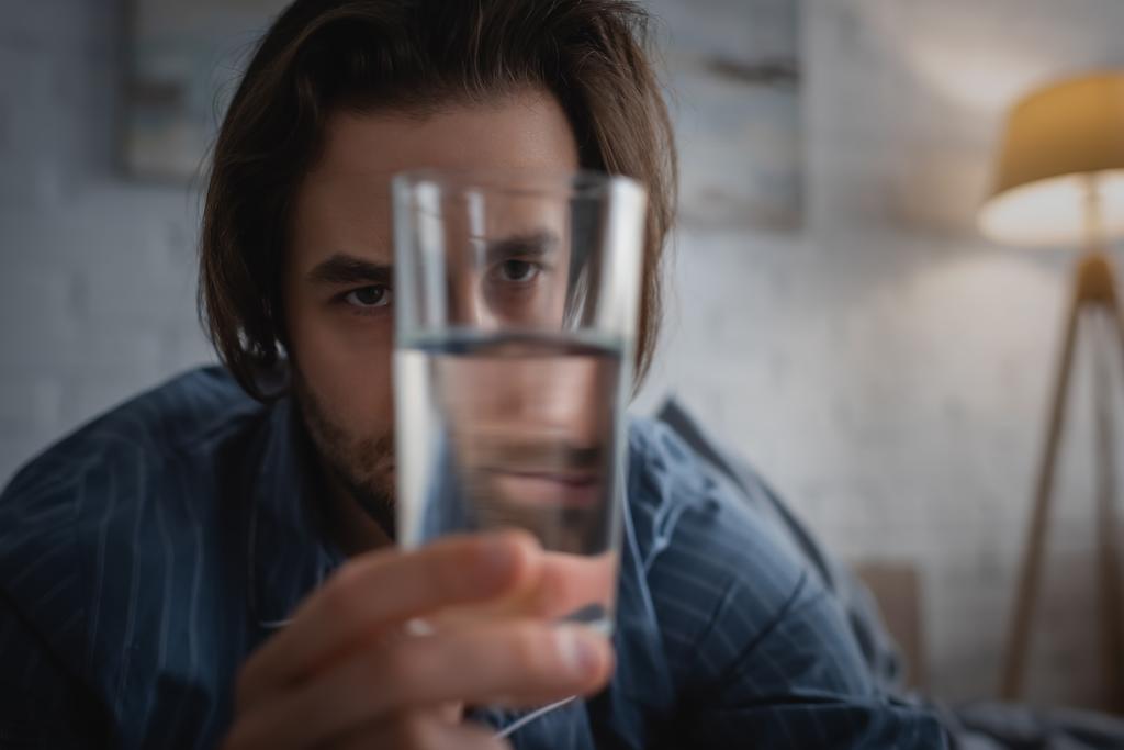 Tired man with sleep disorder holding glass of water at home  - Photo, Image