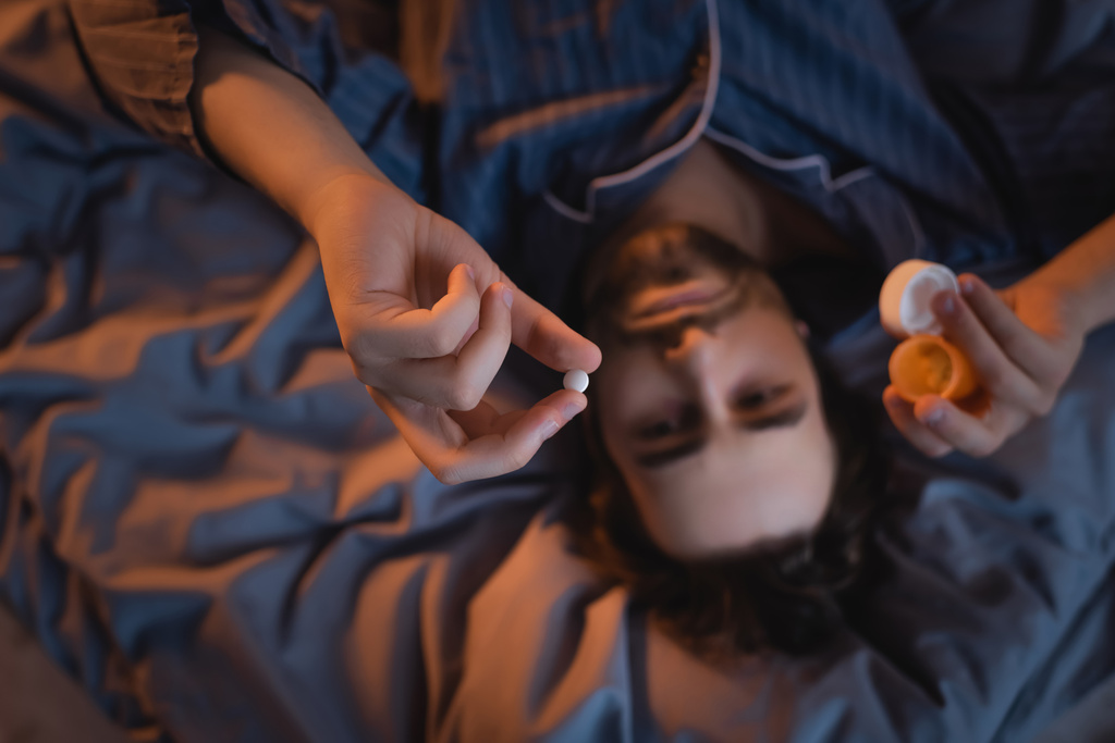 Vue du dessus de l'homme flou tenant la pilule sur le lit la nuit  - Photo, image