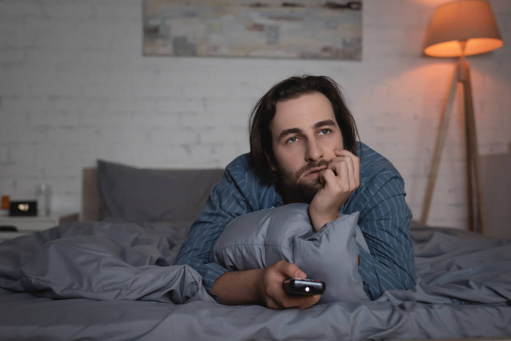 Чоловік з розладом сну дивиться фільм на ліжку вночі
  - Фото, зображення