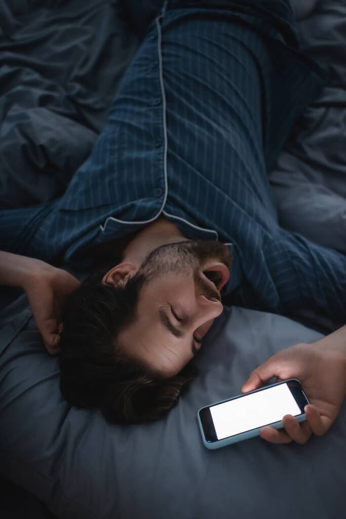 Вид зверху виснажений чоловік позіхає і тримає смартфон на ліжку вдома
  - Фото, зображення