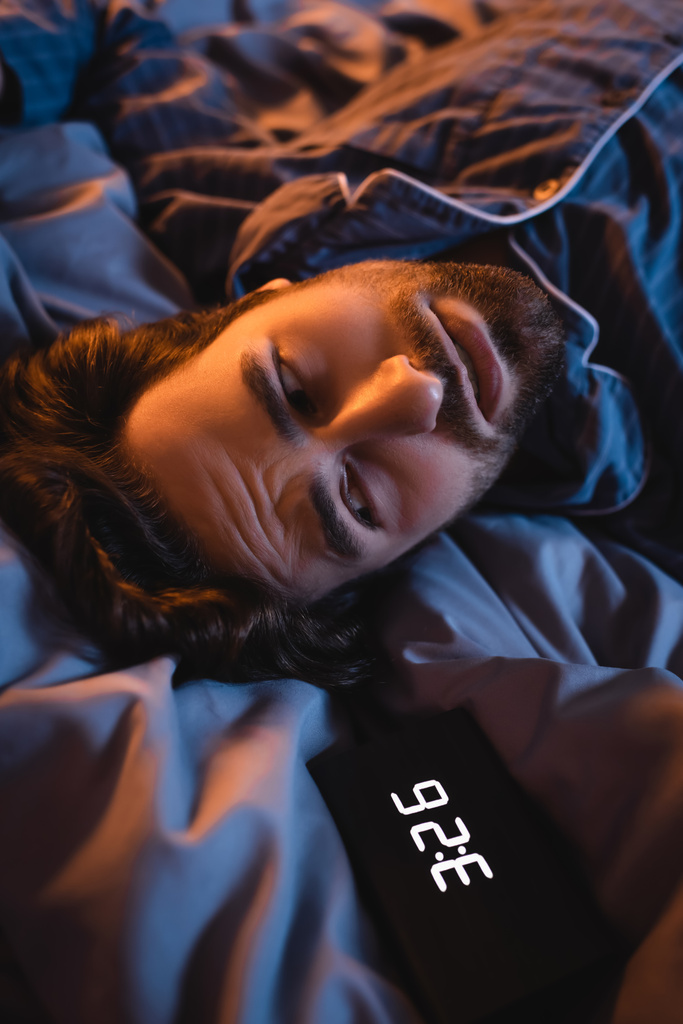 Worried man looking at alarm clock on bed at night  - Fotó, kép