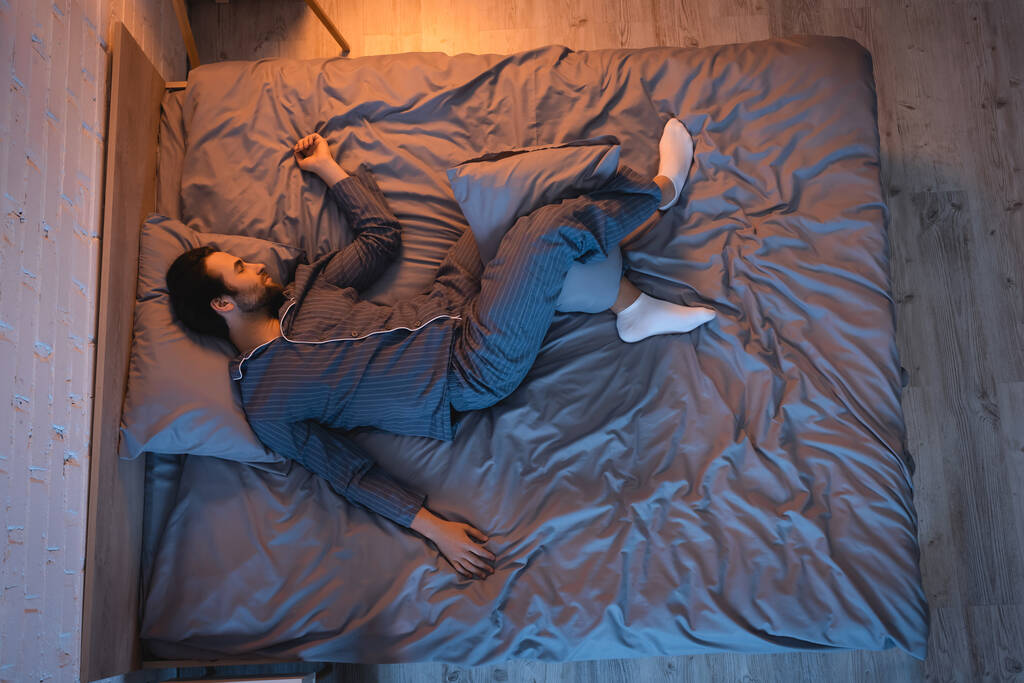 Boční pohled na muže spícího na posteli v ložnici s osvětlením doma  - Fotografie, Obrázek