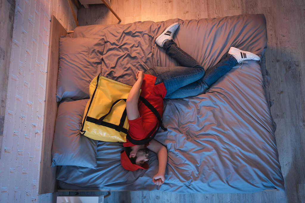 Vue latérale du somnambule en uniforme de livraison dormant sur le lit à la maison  - Photo, image
