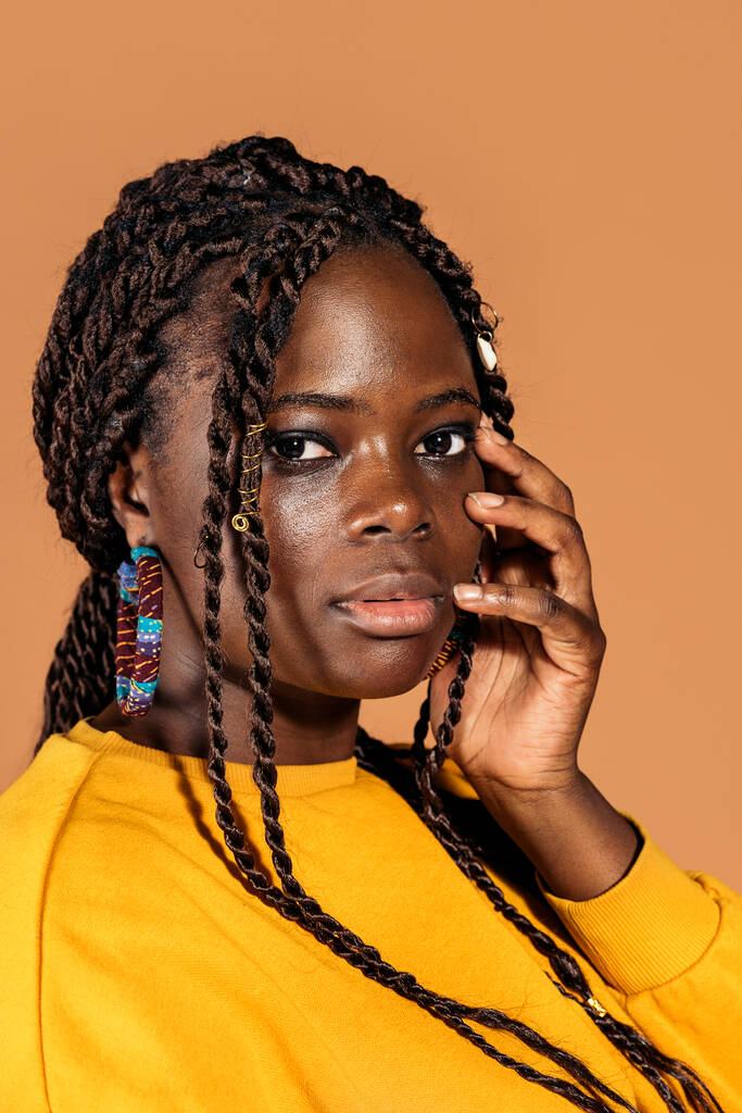 Archivfoto einer selbstbewussten schwarzen Frau mit Zöpfen, die im Studio vor braunem Hintergrund posiert. - Foto, Bild