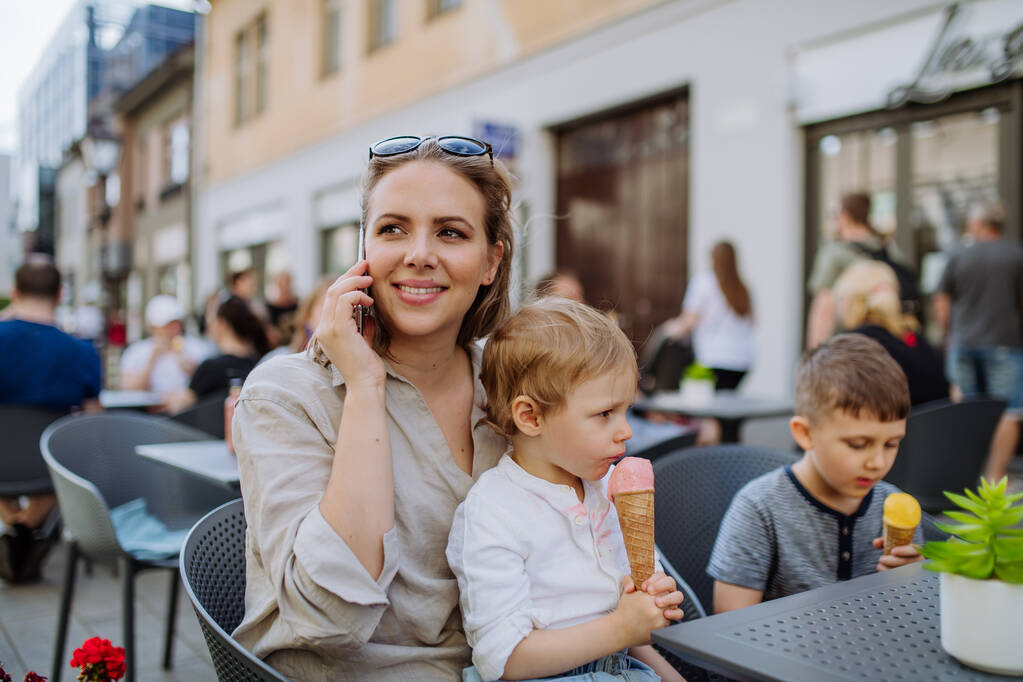Eine junge Mutter macht ein Selfie mit ihren Kindern, die im Sommer in einem Café auf der Straße Eis essen. - Foto, Bild