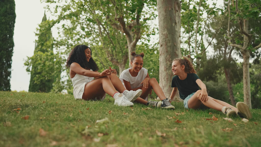 Három tinédzser barát ül a füvön a parkban, és érzelmileg beszélgetnek. Három tinédzser a szabadban - Fotó, kép
