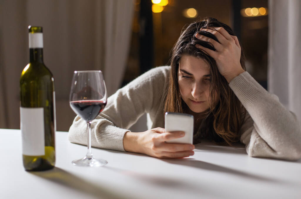 alcoholism, alcohol addiction and people concept - drunk woman or female alcoholic with smartphone drinking red wine at home - Photo, Image
