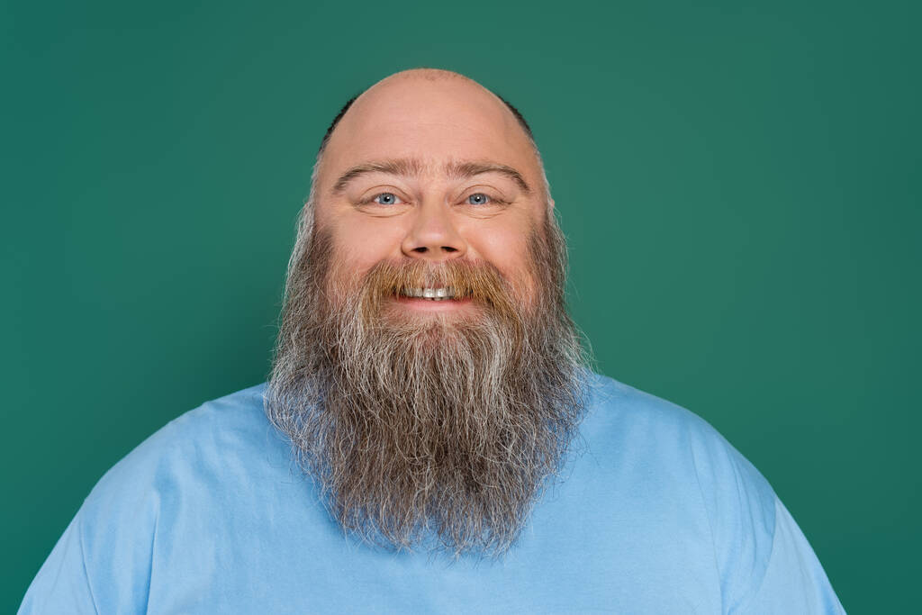 пухлый и лысый мужчина с бородой улыбается в камеру изолированы на зеленый - Фото, изображение