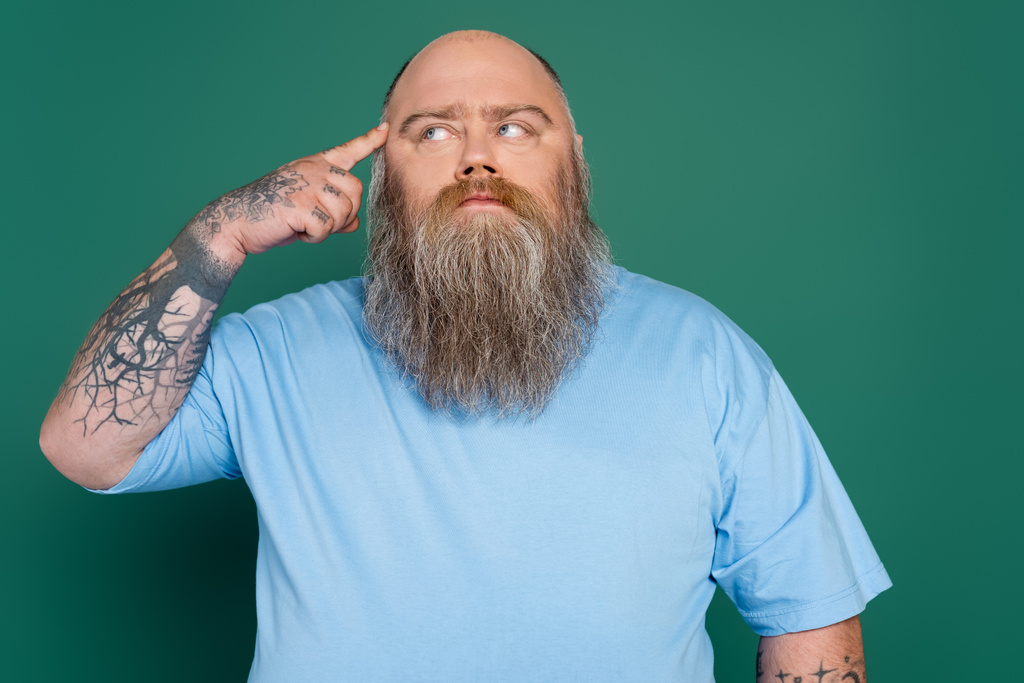 tatuaż plus rozmiar mężczyzna dotykając głowy i patrząc daleko podczas myślenia odizolowany na zielono - Zdjęcie, obraz