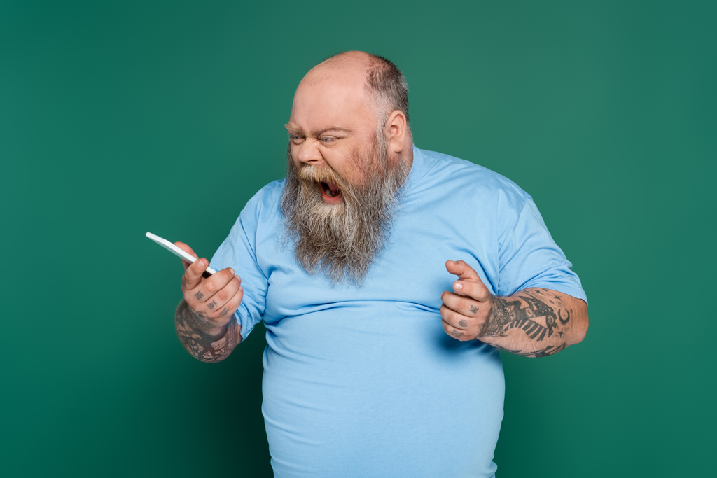 podrážděný nadváha muž křičí při odesílání hlasové zprávy na smartphone izolované na zelené - Fotografie, Obrázek