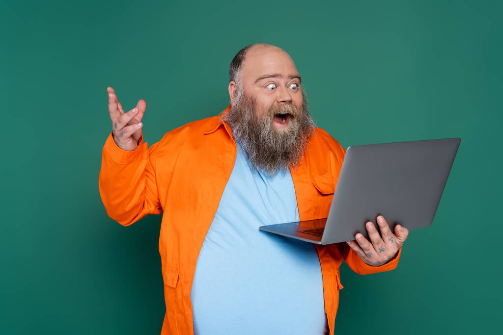 amazed overweight man with beard looking at laptop isolated on green - Fotografie, Obrázek