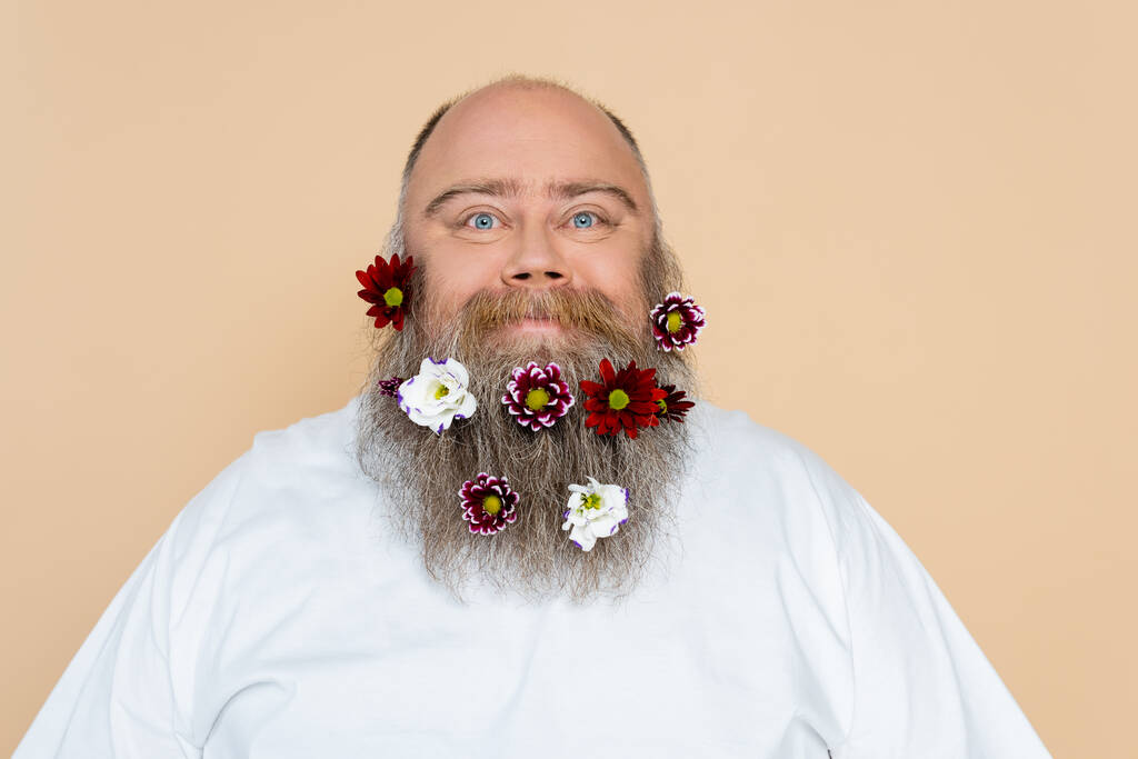 positive overweight man with floral decor in beard looking at camera isolated on beige - Zdjęcie, obraz
