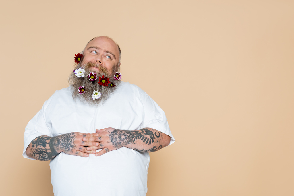 pleased overweight man with flowers in beard and hands on tummy isolated on beige - Foto, Imagen
