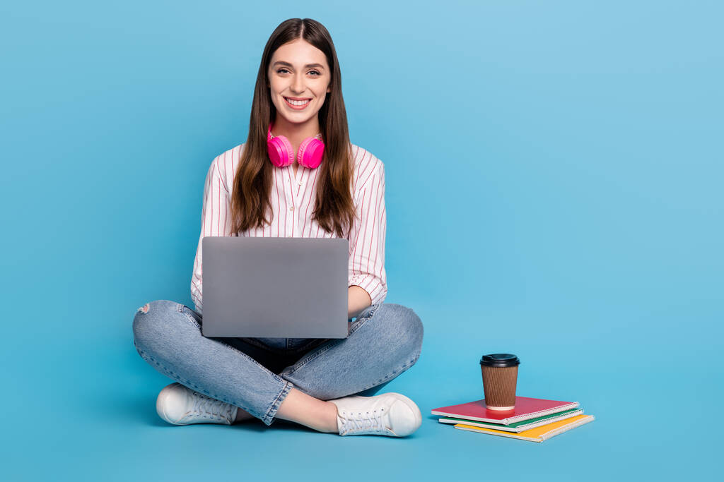 Портрет привлекательной веселой девушки, сидящей на ноутбуке и дистанционно изолированной на ярко-голубом фоне. - Фото, изображение
