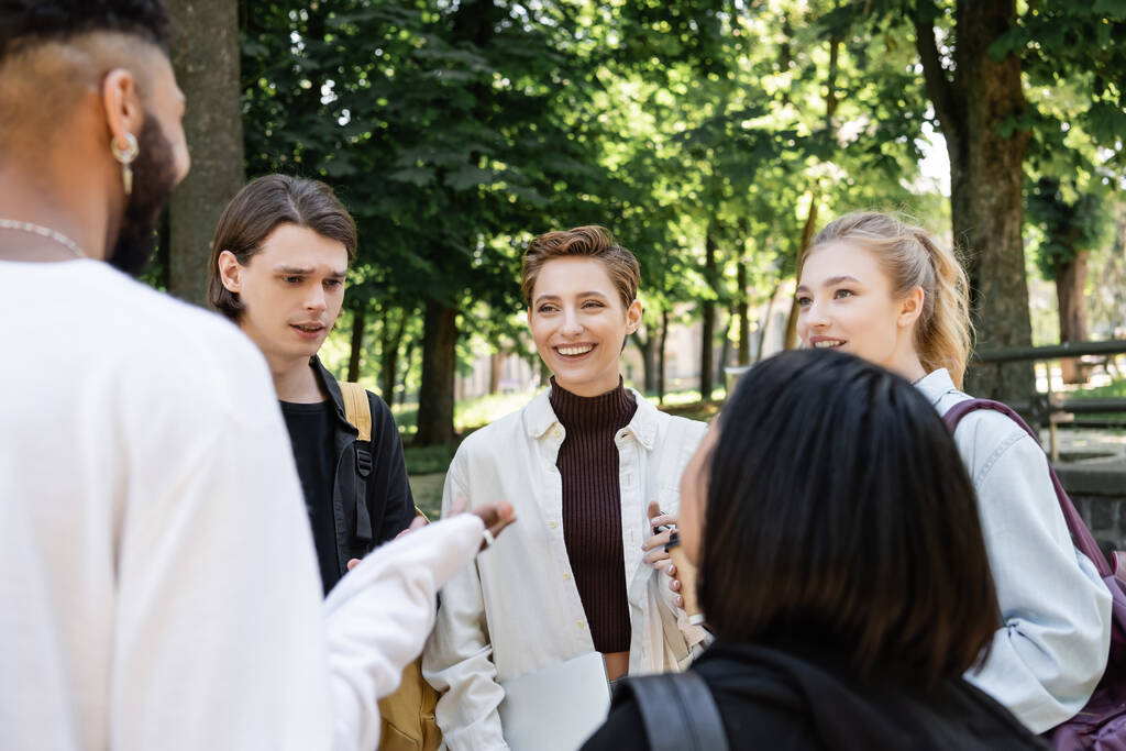 Positive students looking at blurred interracial friends in summer park  - Fotó, kép