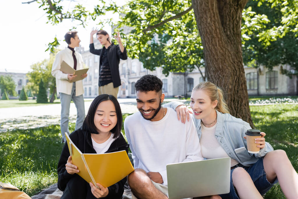 Азійські студенти тримають записник поруч з друзями з ноутбуком і кавою в парку.  - Фото, зображення