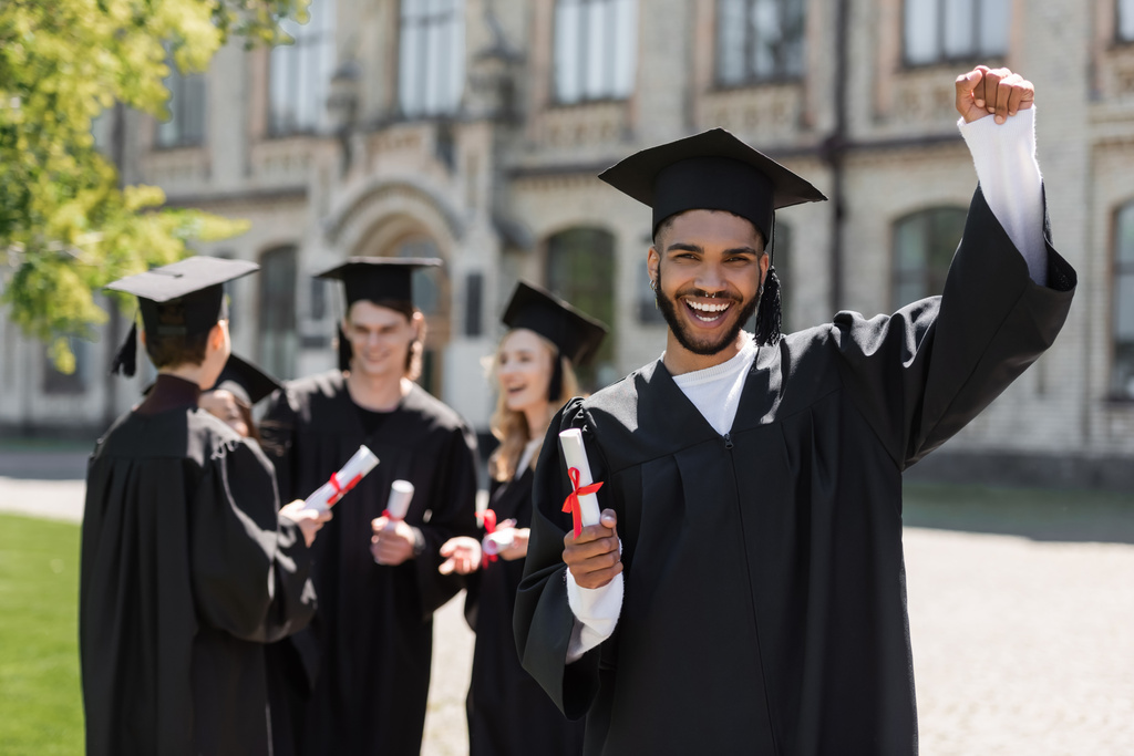 Excited african american bachelor holding diploma near friends in park  - Photo, Image