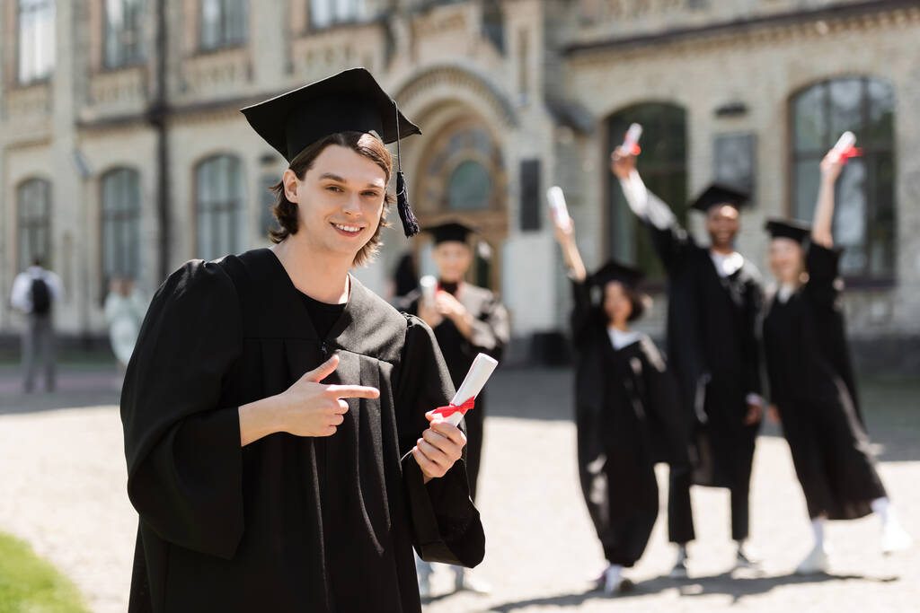 Bachelor in cap pointing at diploma outdoors  - Valokuva, kuva