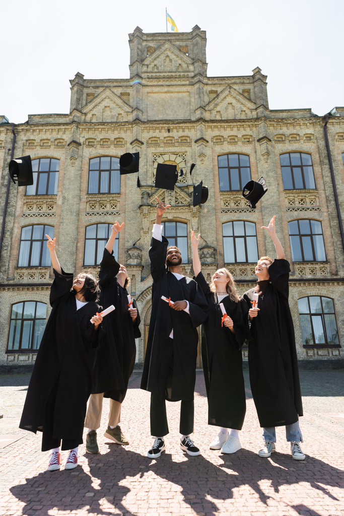 Позитивні міжрасові холостяки з дипломами кидають шапки біля університету на відкритому повітрі
  - Фото, зображення