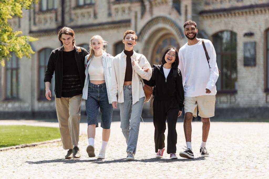 Jovens estudantes multiétnicos caminhando e olhando para a câmera perto da universidade ao ar livre  - Foto, Imagem