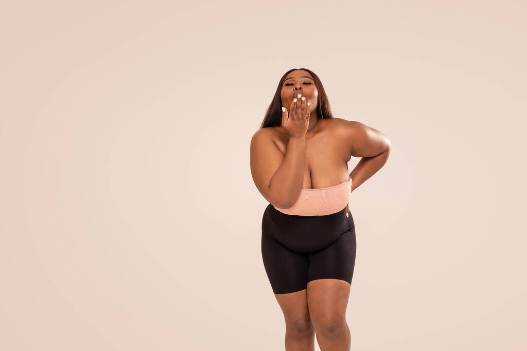 Happy, attractive, plus size, dark skinned woman sending kisses, posing in studio. Beauty portrait. Concept of body acceptance, body positivity. Girl power - Photo, Image