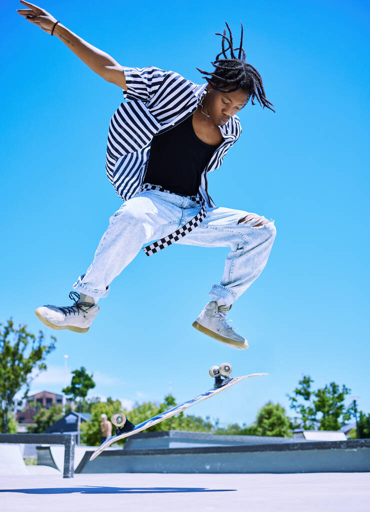 Super mladý chlapec předvádí triky na svém skateboardu v skateparku. Soustředěný mladý Afroameričan vyskočil a vyhodil skateboard do vzduchu. Stylový mladý bruslař těší park. - Fotografie, Obrázek
