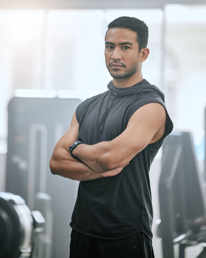 Portrait of one serious asian trainer alone in gym. Handsome focused coach standing with arms crossed after workout in health club. Young confident man in fitness centre for routine training exercise. - Photo, image