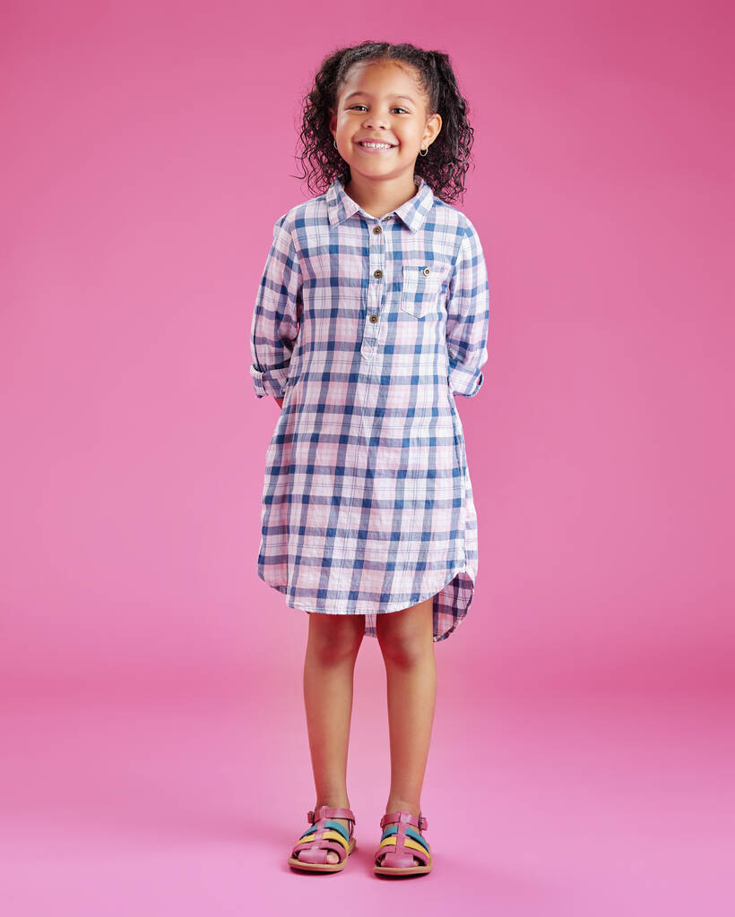 Een portret van een mooi klein gemengd ras meisje met krullend haar poseren tegen een roze copyspace achtergrond in een studio. Een lachend Afrikaans kind dat casual kleding draagt binnen. - Foto, afbeelding