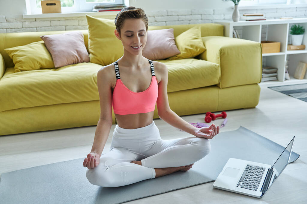 Schöne junge Frau in Sportkleidung meditiert zu Hause - Foto, Bild