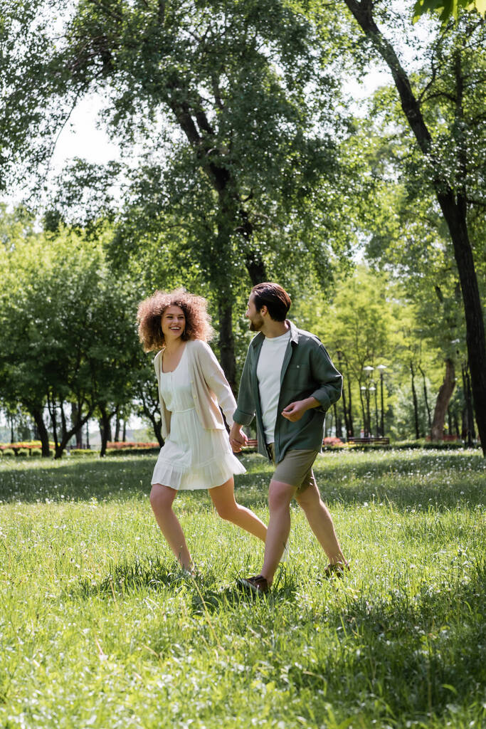 πλήρες μήκος των χαρούμενα νεαρό ζευγάρι που έχουν ημερομηνία, ενώ το περπάτημα στο πράσινο πάρκο  - Φωτογραφία, εικόνα