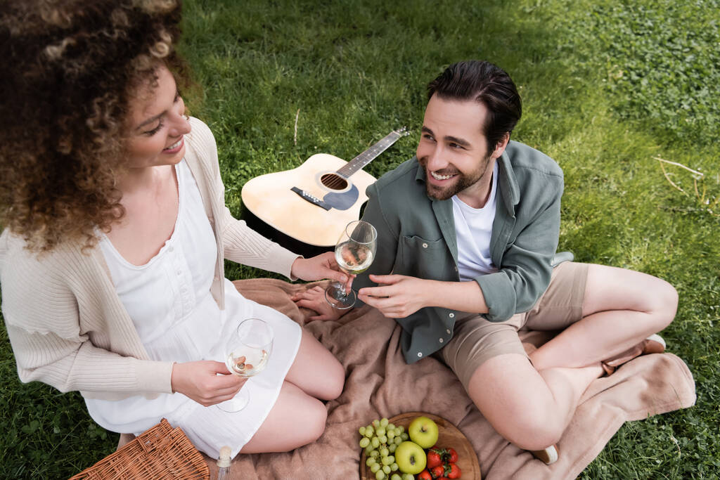 high angle view of happy curly woman passing glass of wine to boyfriend during summer picnic - Foto, afbeelding