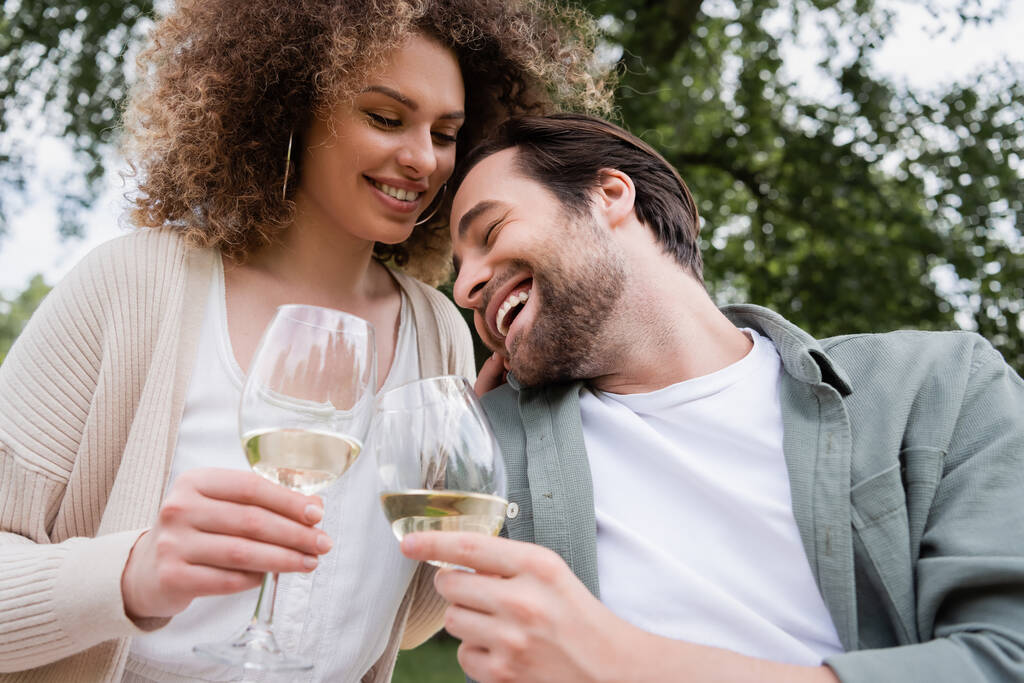 happy man and cheerful woman holding glasses of wine in park - Fotoğraf, Görsel