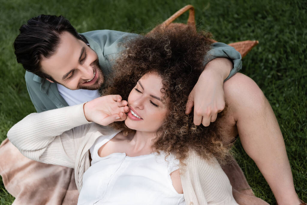 top view of curly woman lying on happy boyfriend during picnic in summer park  - Foto, afbeelding