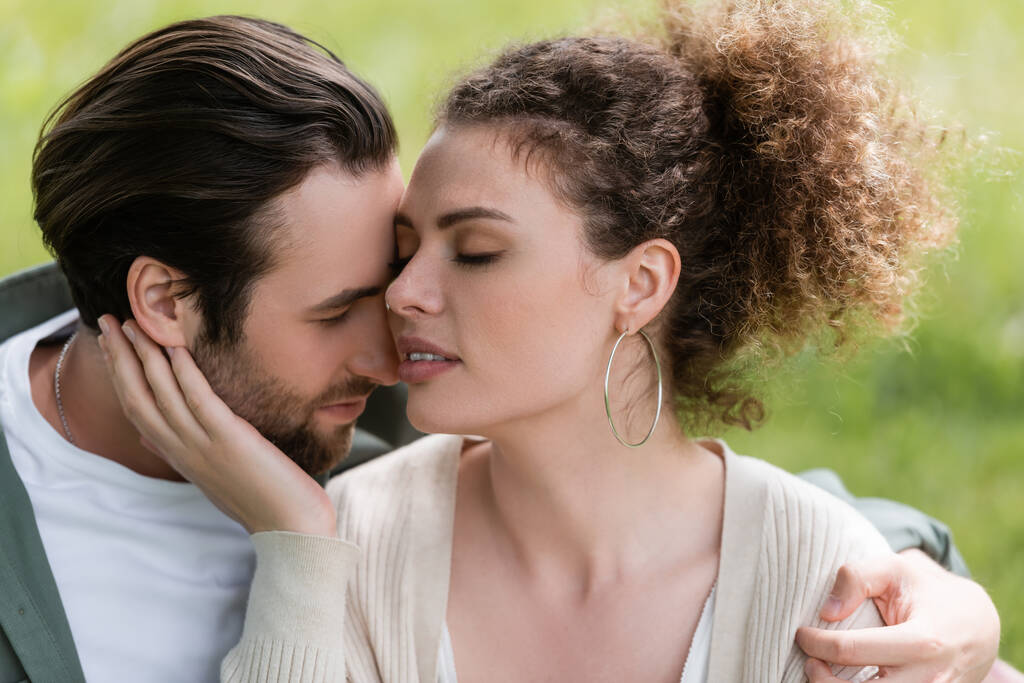 tender and curly woman touching face of bearded man in park - Fotoğraf, Görsel