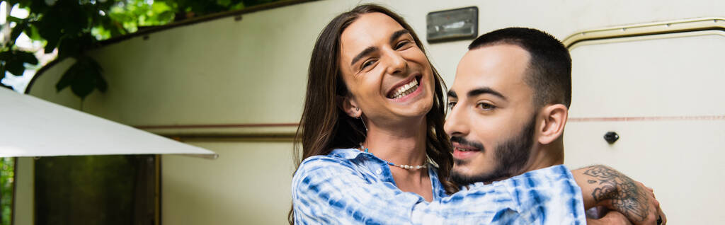 happy tattooed gay man hugging cheerful boyfriend near travel van, banner - Photo, image